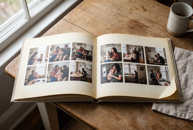 Open family photo book on a wooden table showing a grid of candid home photographs