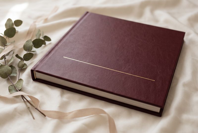 Burgundy leather photo book with a single gold foil line, on cream silk with eucalyptus